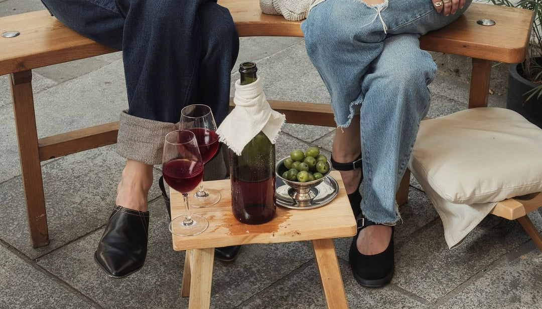 Zwei Gläser gekühlter Rotwein, eine Flasche mit Kühltuch und Oliven auf einem Holzhocker im Freien
